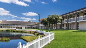 A motel with a pond, white picket fence, and a clear blue sky. - Rodeway Inn At Fort Lee (Hopewell)