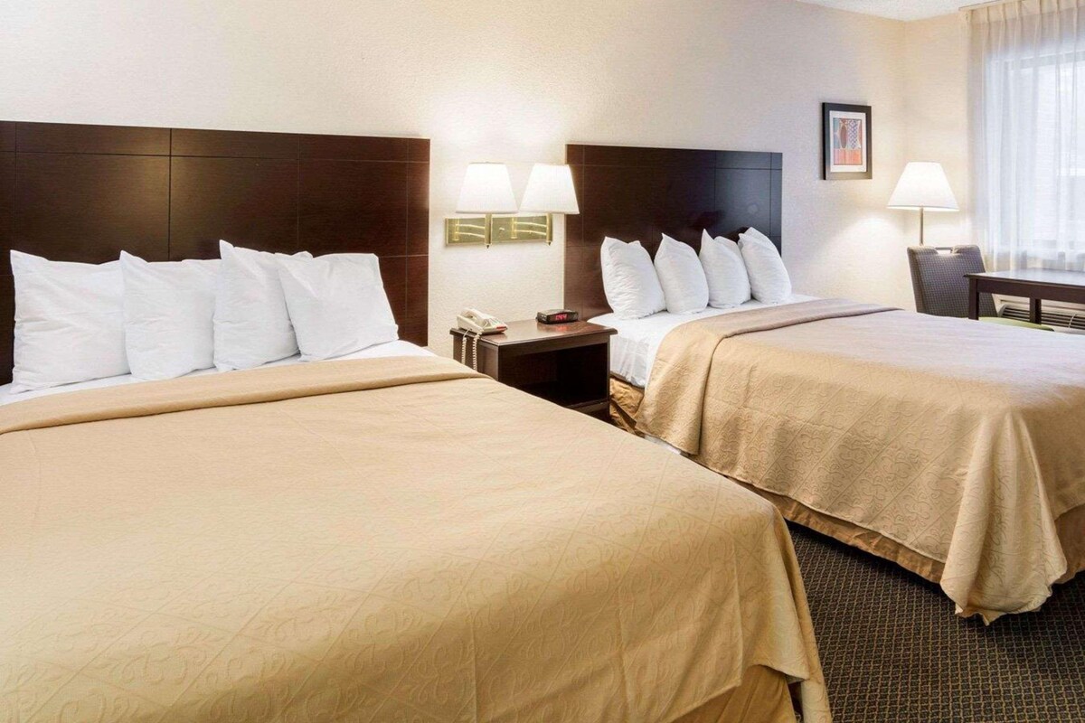 A hotel room with two beds, each with a headboard, bedside tables with lamps, and a framed picture on the wall.