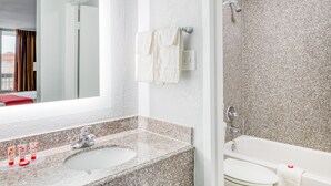 A modern bathroom with a granite countertop sink, a mirror, a shower, and a toilet. - Hotel elev8 (Conroe)