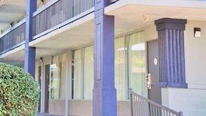 Ein mehrstöckiges Gebäude mit einem Balkon im zweiten Stock, großen Fenstern und einer Tür mit einer Nummer.'