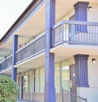 Un edificio de varios pisos con un balcón en el segundo nivel, ventanas grandes y una puerta con una placa de número.