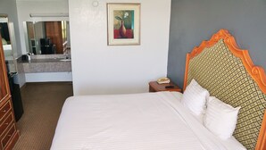 A hotel room with a large bed, a wooden dresser, a nightstand with a telephone, and a painting on the wall. - Hotel elev8 (Conroe)