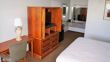 A hotel room with a bed, a wooden dresser, a desk with a lamp, and a mirror.