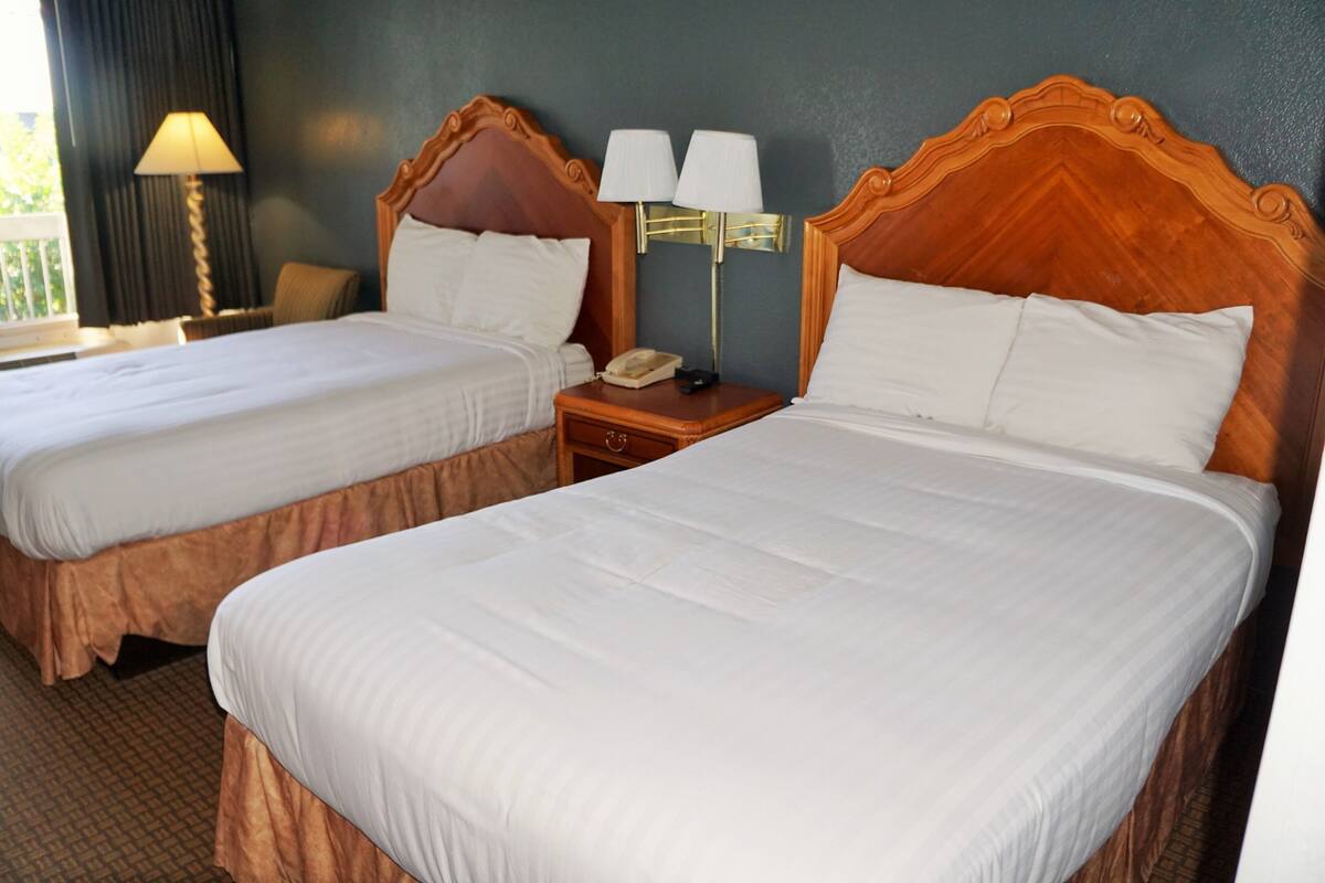 A hotel room with two beds, a nightstand with a lamp, and a telephone.