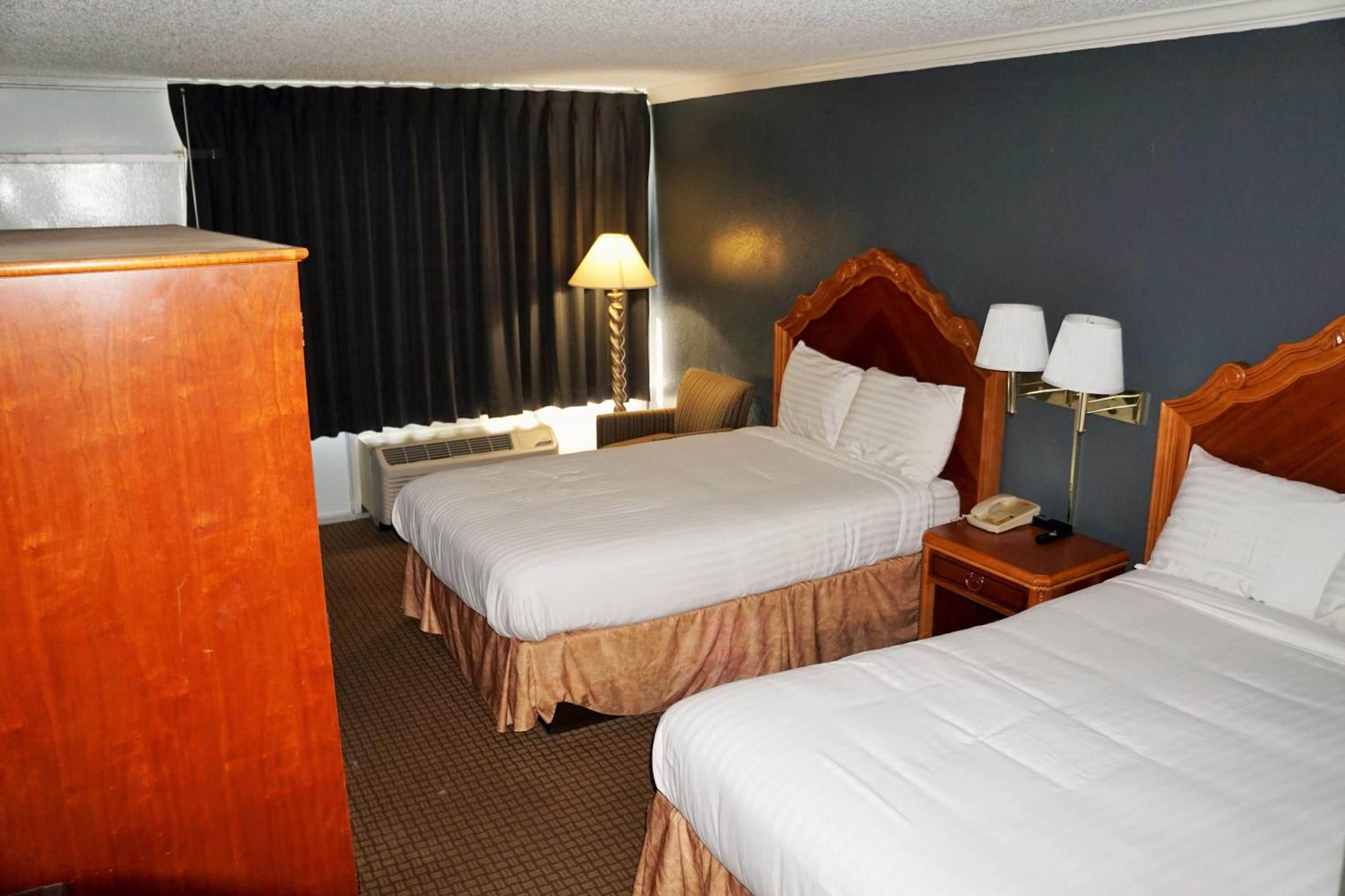 Una habitación de hotel con dos camas, un escritorio, una silla, una lámpara y un teléfono.