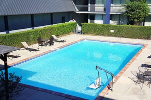 Una piscina rectangular con agua cristalina y azul, rodeada de sillas de descanso y una pequeña mesa.