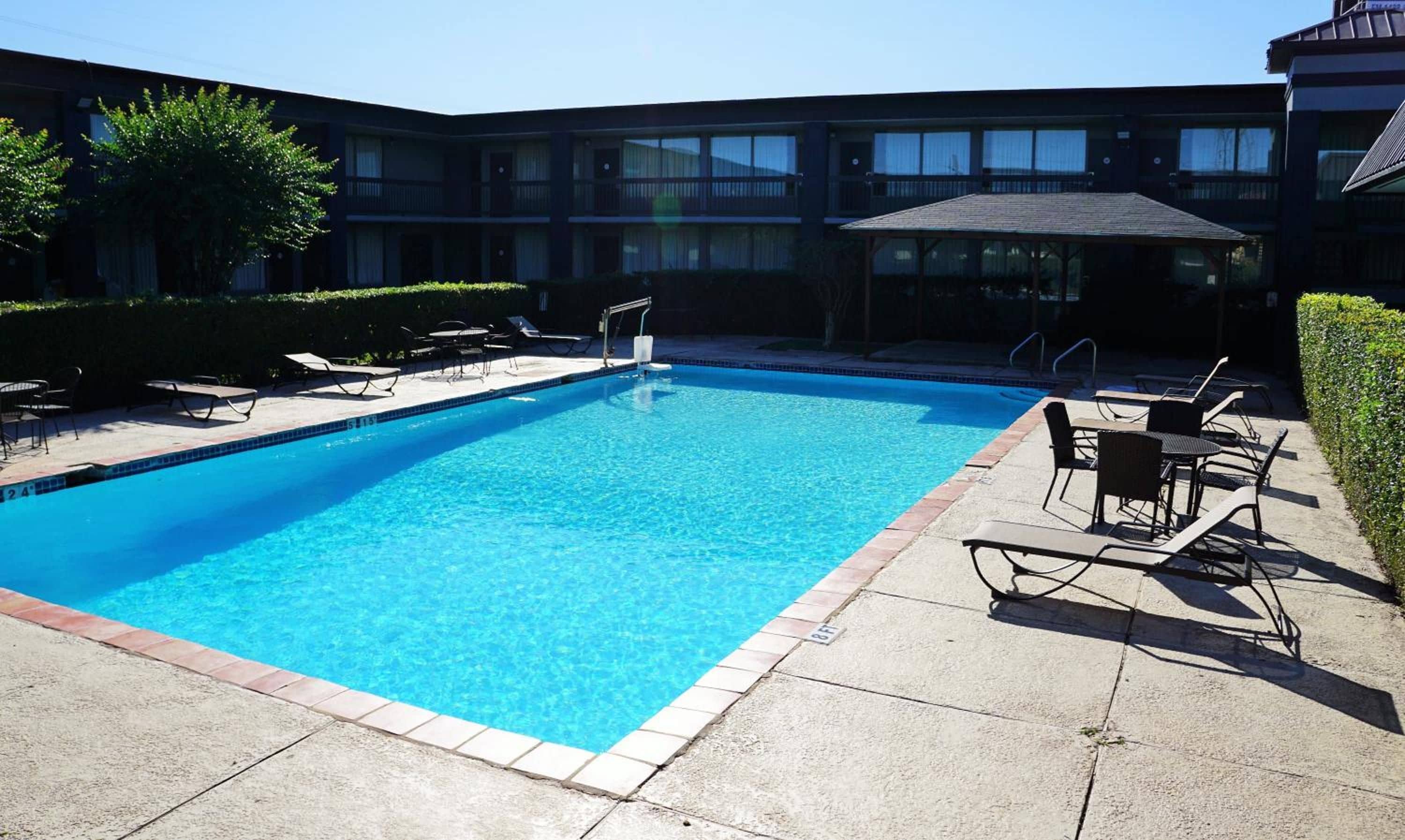 Una piscina rettangolare con bordo piastrellato, circondata da sedie a sdraio e un'area salotto coperta.