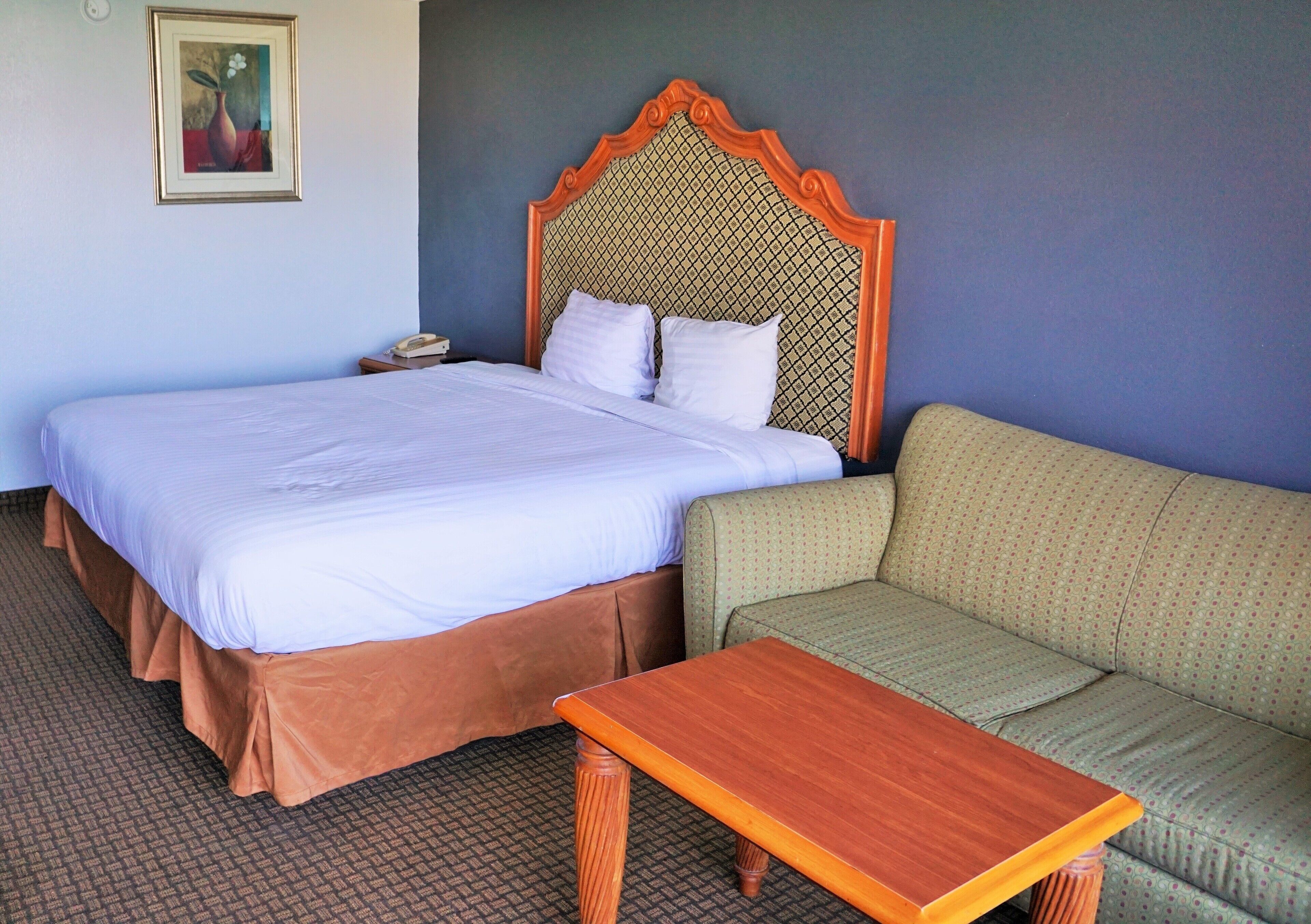 A hotel room with a large bed, a wooden nightstand, a green sofa, and a small wooden table.