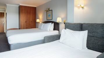 A hotel room with two single beds, a sofa, a wooden wardrobe, and two wall-mounted lamps.