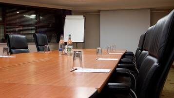 A conference room with a long wooden table, black leather chairs, water bottles, and a whiteboard.