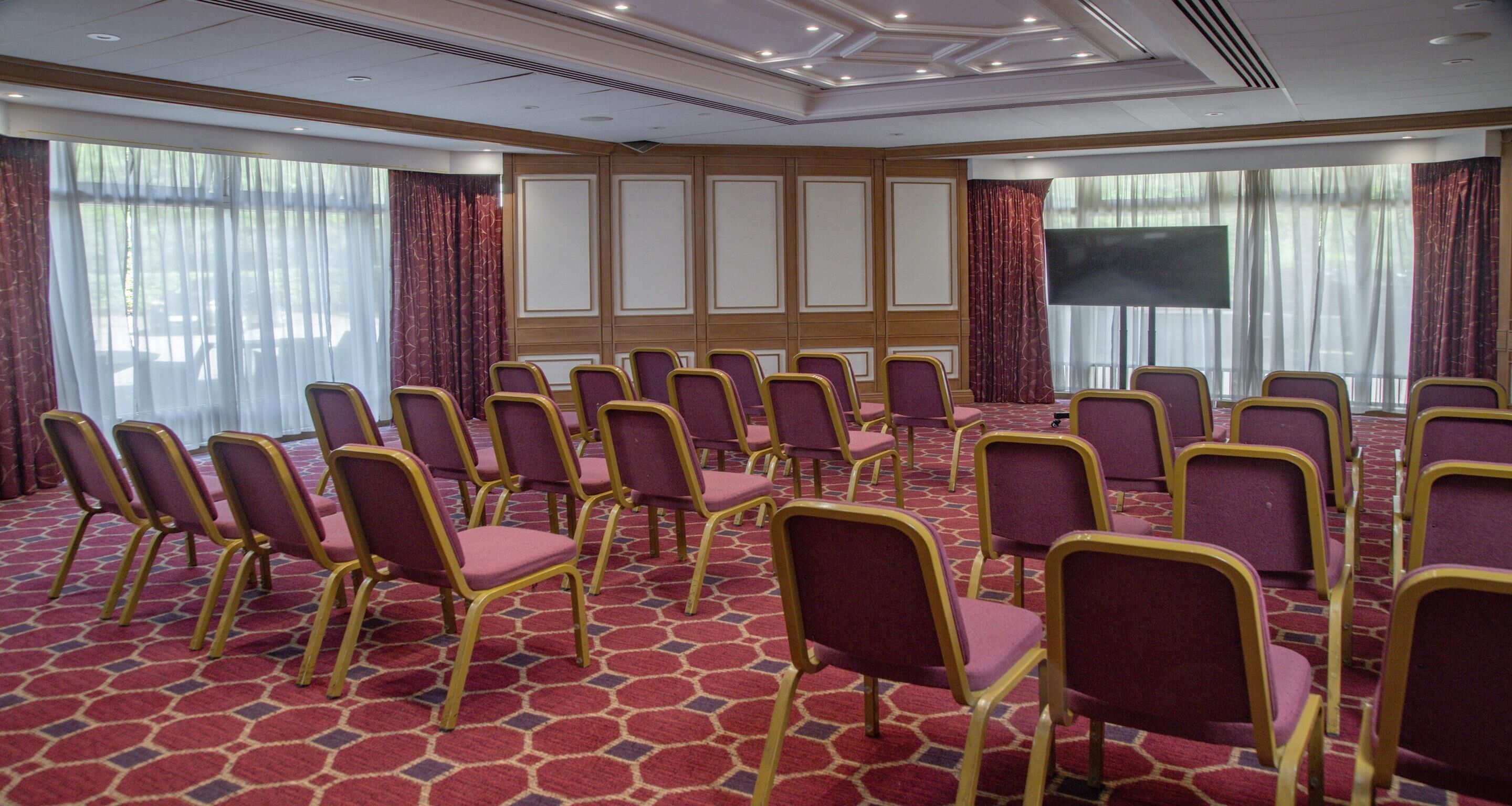 A conference room with rows of purple chairs and a large screen.