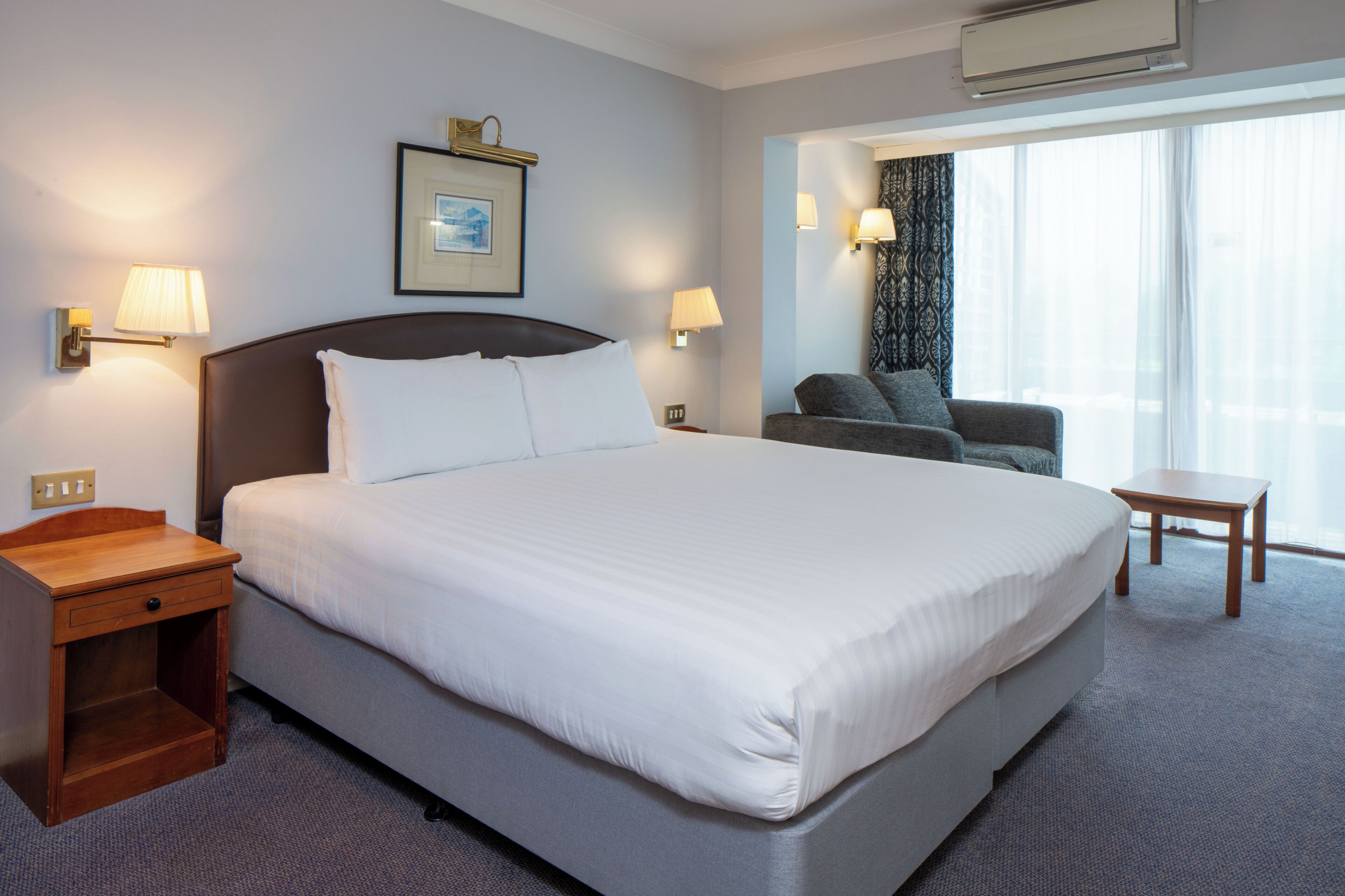 Una habitación de hotel con una cama grande, mesitas de noche, una silla y una pequeña mesa.