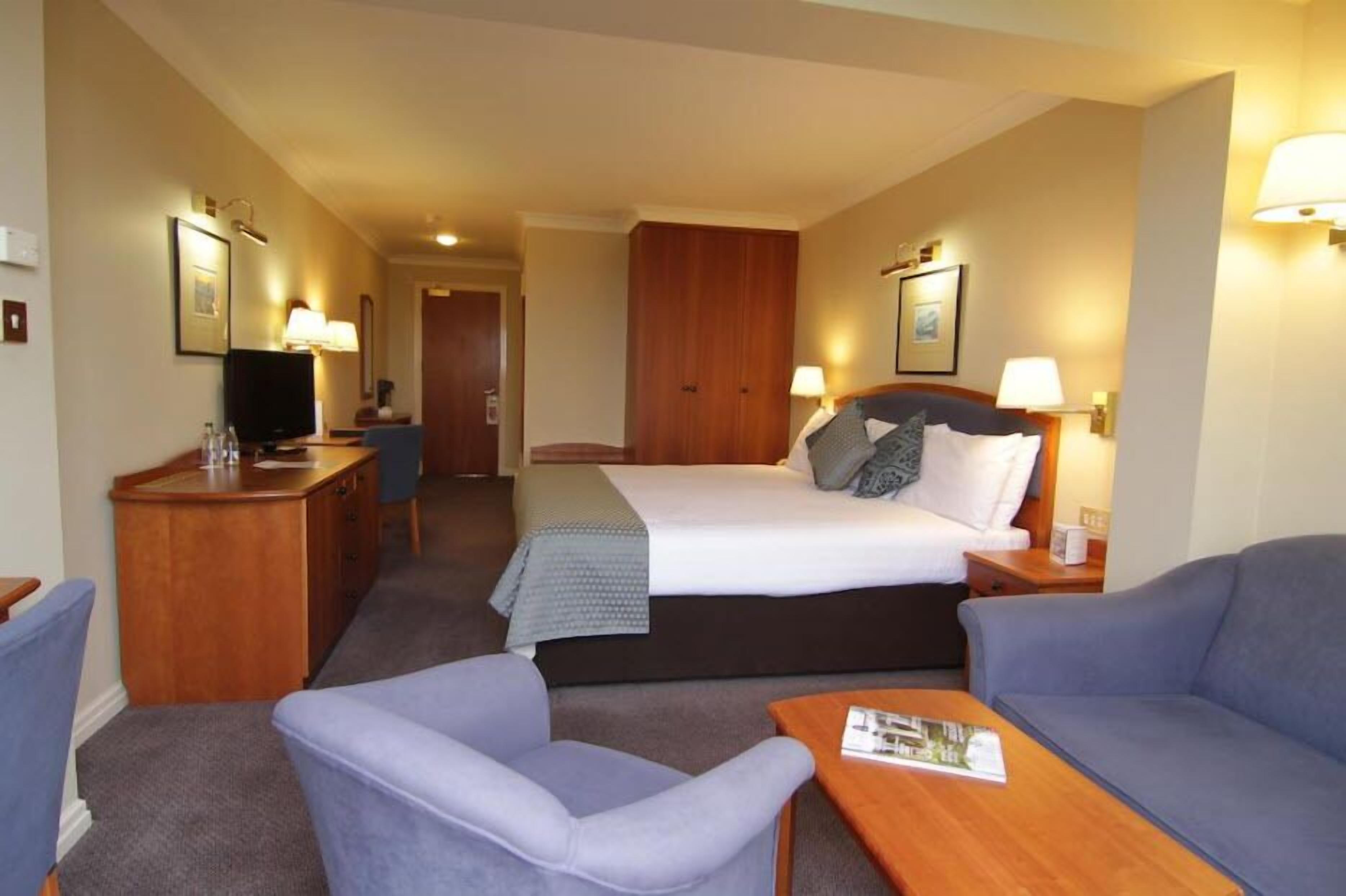 A hotel room with a bed, two bedside tables, a desk with a chair, a sofa, and a television.