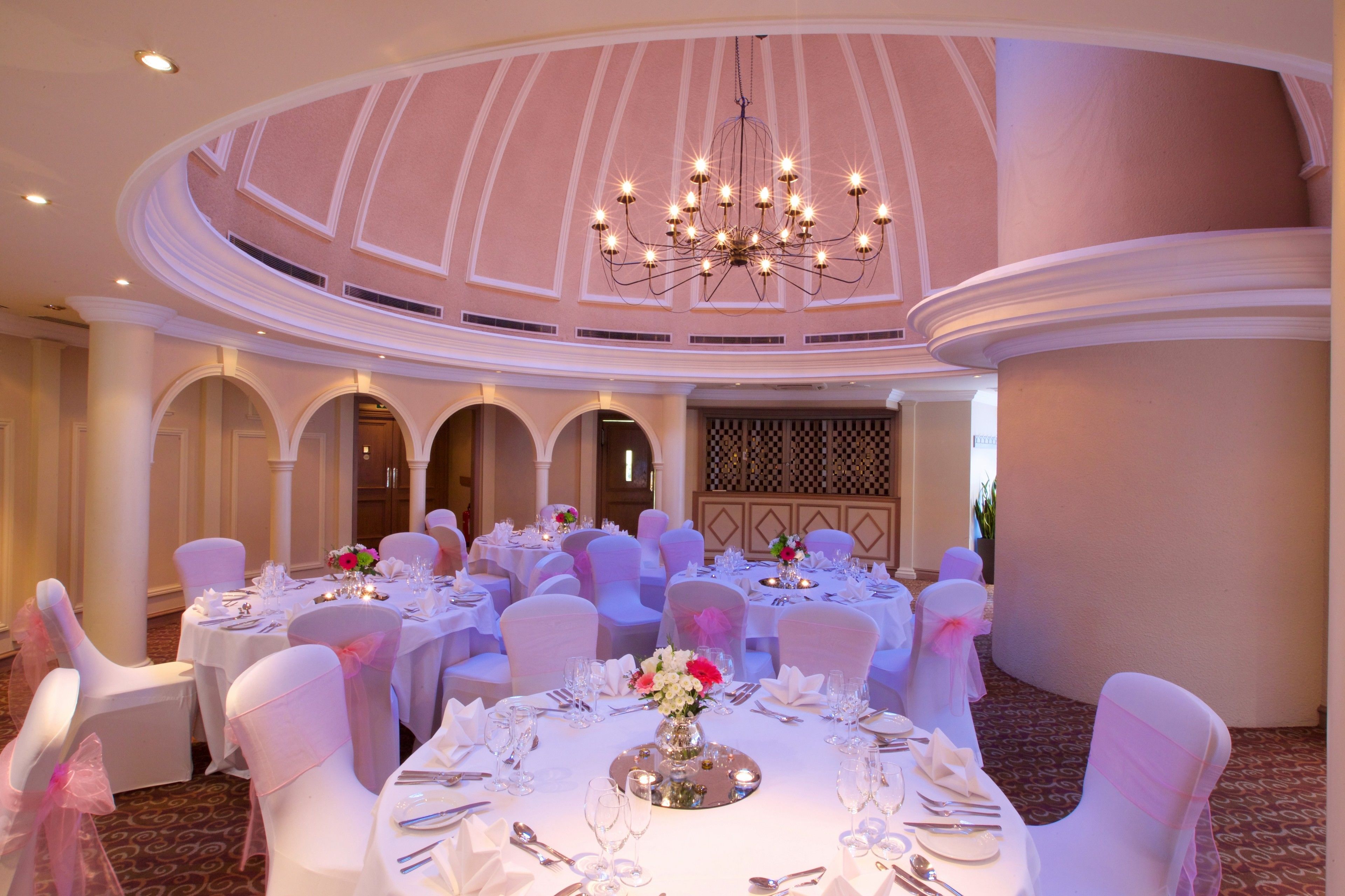 A banquet hall with round tables, white chairs, and a chandelier.