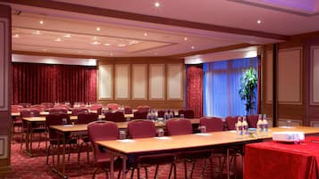 A conference room with multiple tables and chairs, a projector, and a red carpeted floor.
