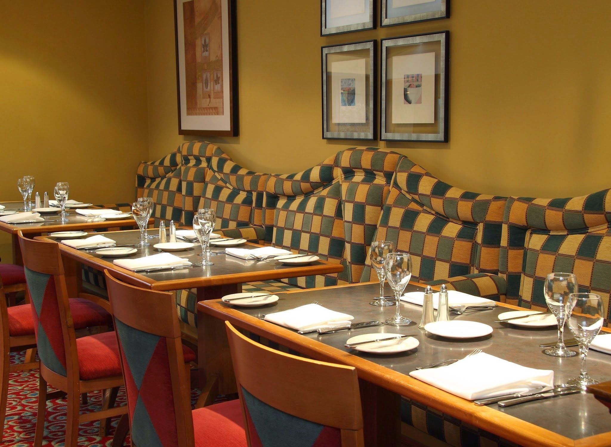 A dining area with a long table set for multiple guests, chairs with red cushions, and framed artwork on the wall.