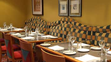 Un comedor con una mesa larga dispuesta para varios comensales, sillas con cojines rojos y cuadros en la pared.