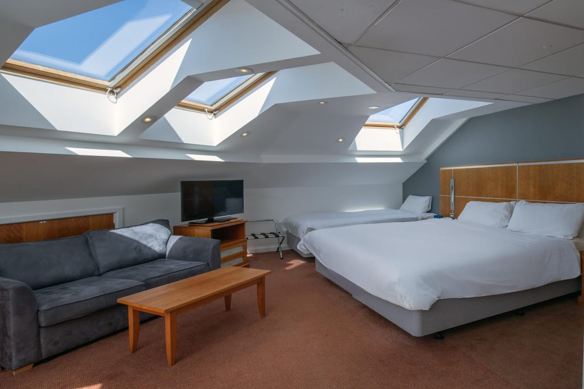 Una habitación de hotel moderna con una cama grande, un sofá, un escritorio y tragaluces.