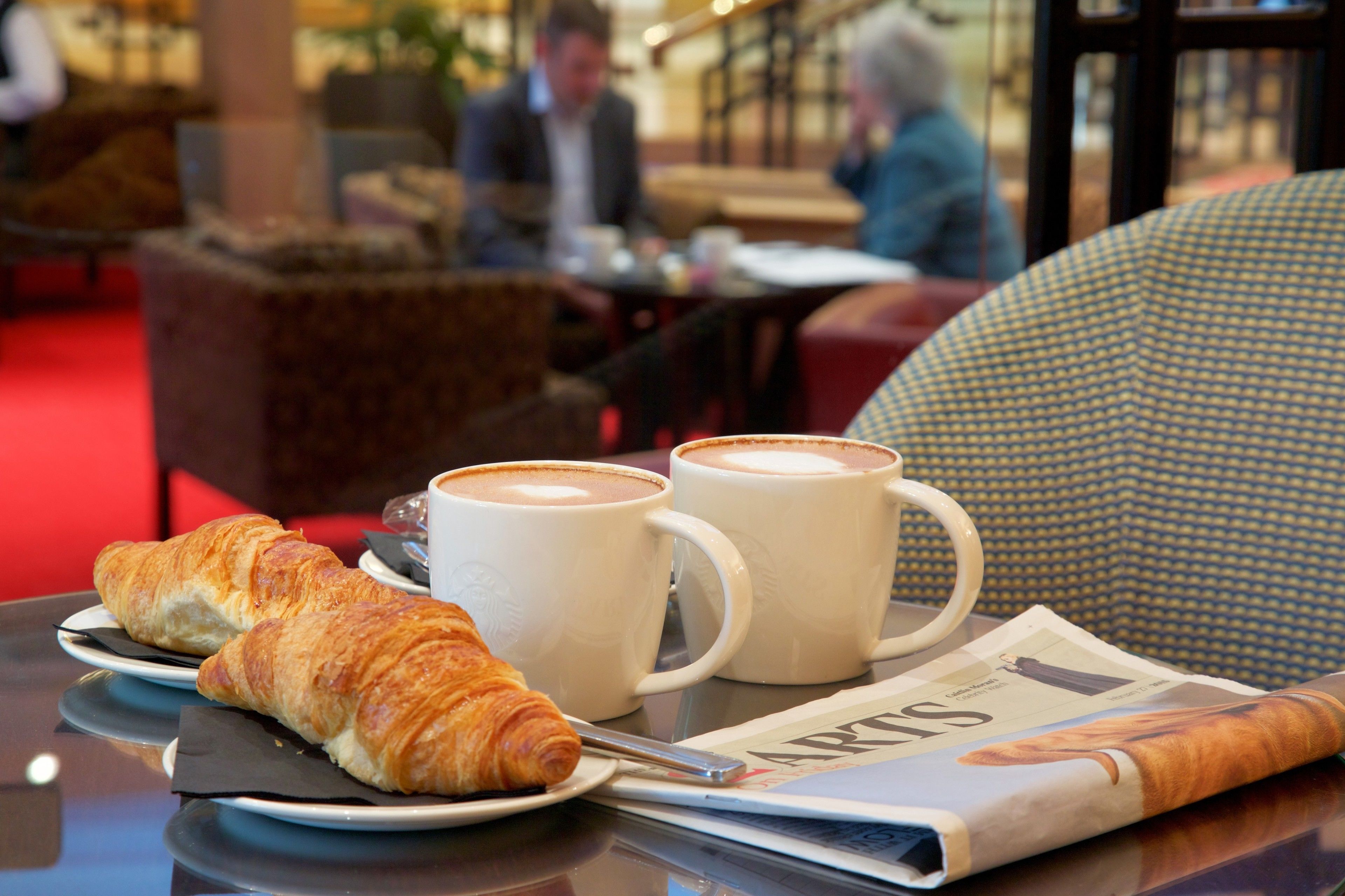 Ein Tisch mit Croissants, Kaffeetassen und einer Zeitung.