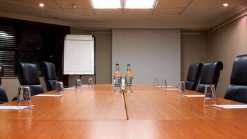 Un salón de conferencias con una larga mesa de madera, sillas de cuero negro, una pantalla de proyector y dos botellas de agua.