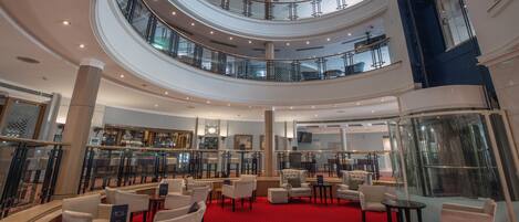 A multi-level hotel lobby with a red carpet, seating areas, and a bar.