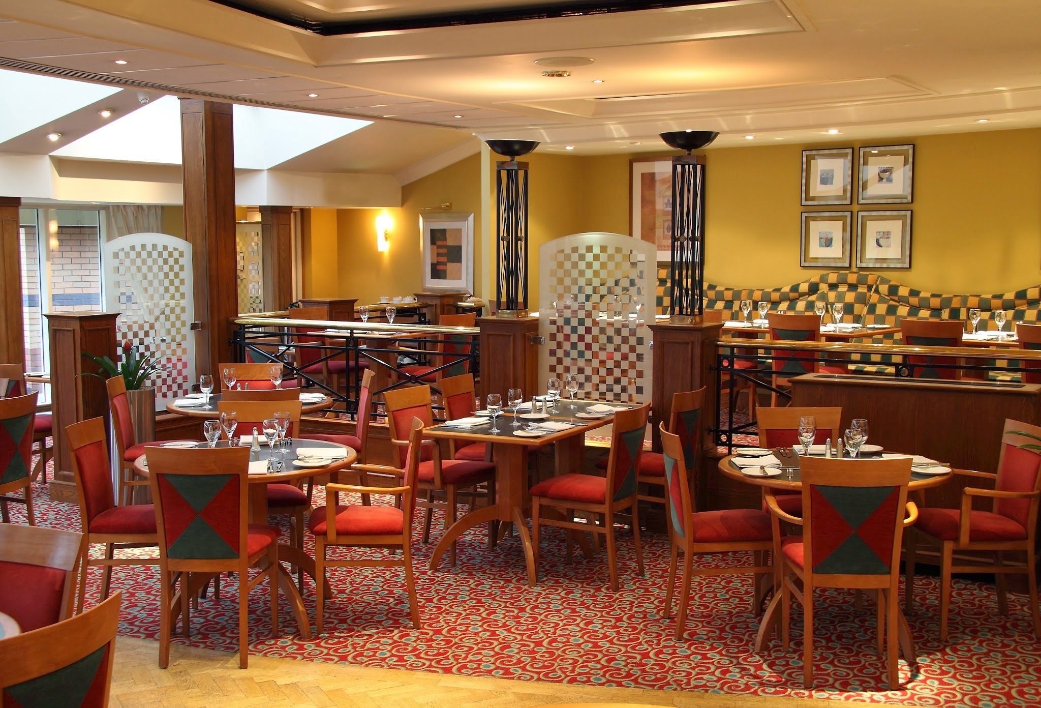 A restaurant with checkered patterned walls, red and green upholstered chairs, and a patterned carpet.