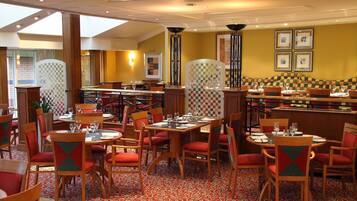 A restaurant with checkered patterned walls, red and green upholstered chairs, and a patterned carpet.