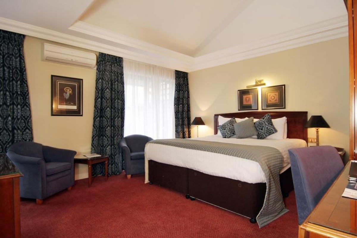 A hotel room with a large bed, two chairs, a small table, and a desk.