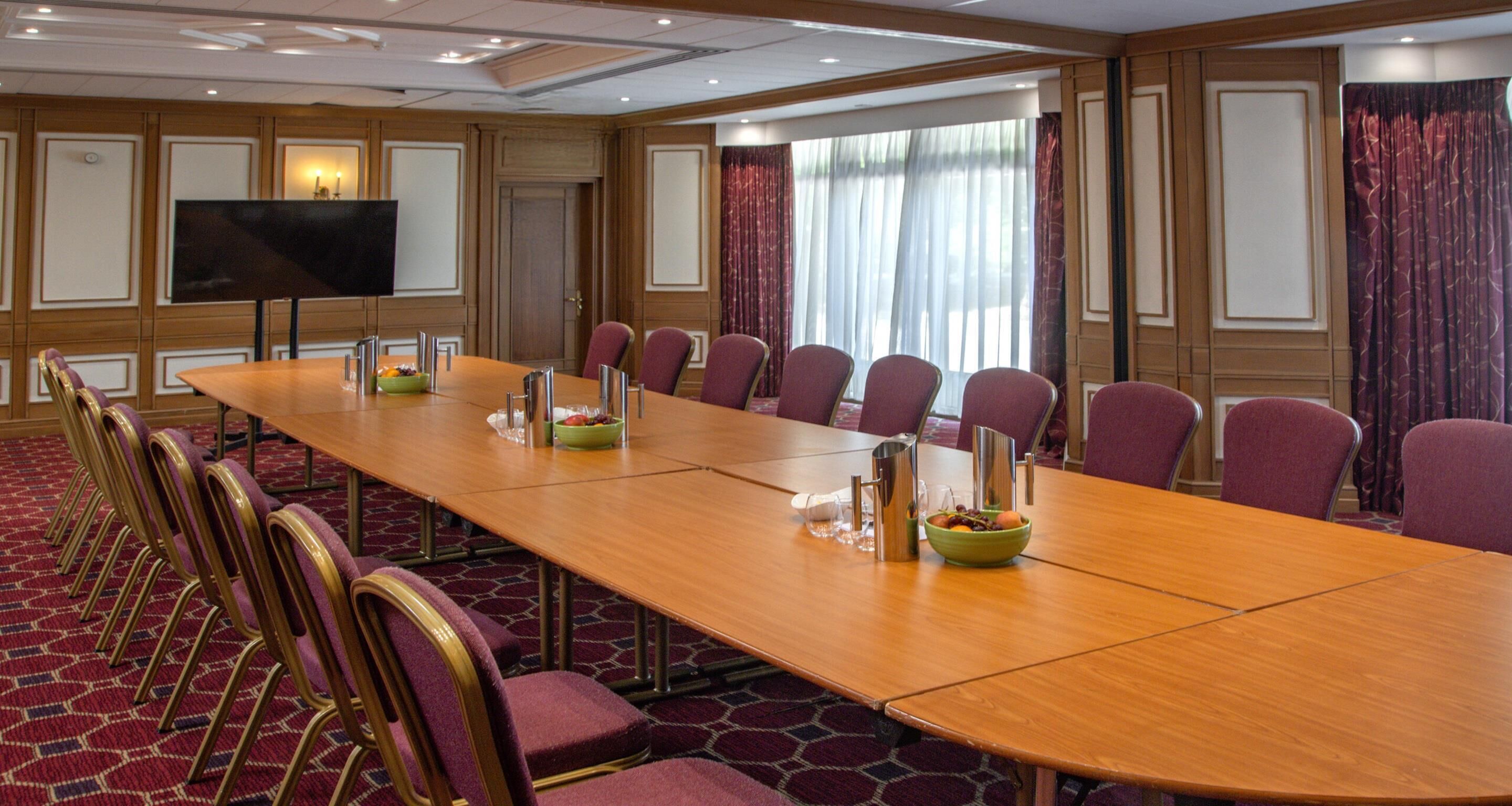 A conference room with a long table, multiple chairs, a TV, and a window with curtains.