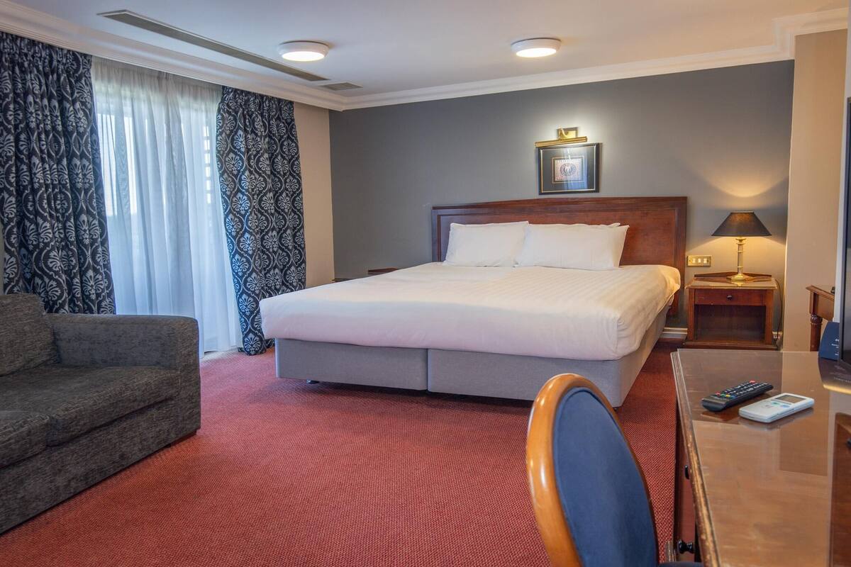 Habitación de hotel con cama, sofá, escritorio y televisor, además de una lámpara.