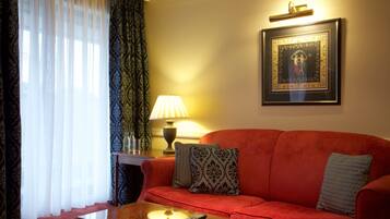 Ein Wohnzimmer mit einem roten Sofa, gemusterten Kissen, einem Glastisch, einer Lampe und einem gerahmten Bild an der Wand.