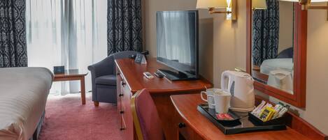 A hotel room with a bed, a desk with a computer, a chair, a television, a coffee maker, and a tray with breakfast items.