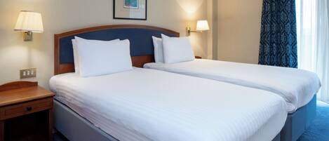 A hotel room with two beds, a nightstand, a lamp, an air conditioning unit, and a window with curtains.