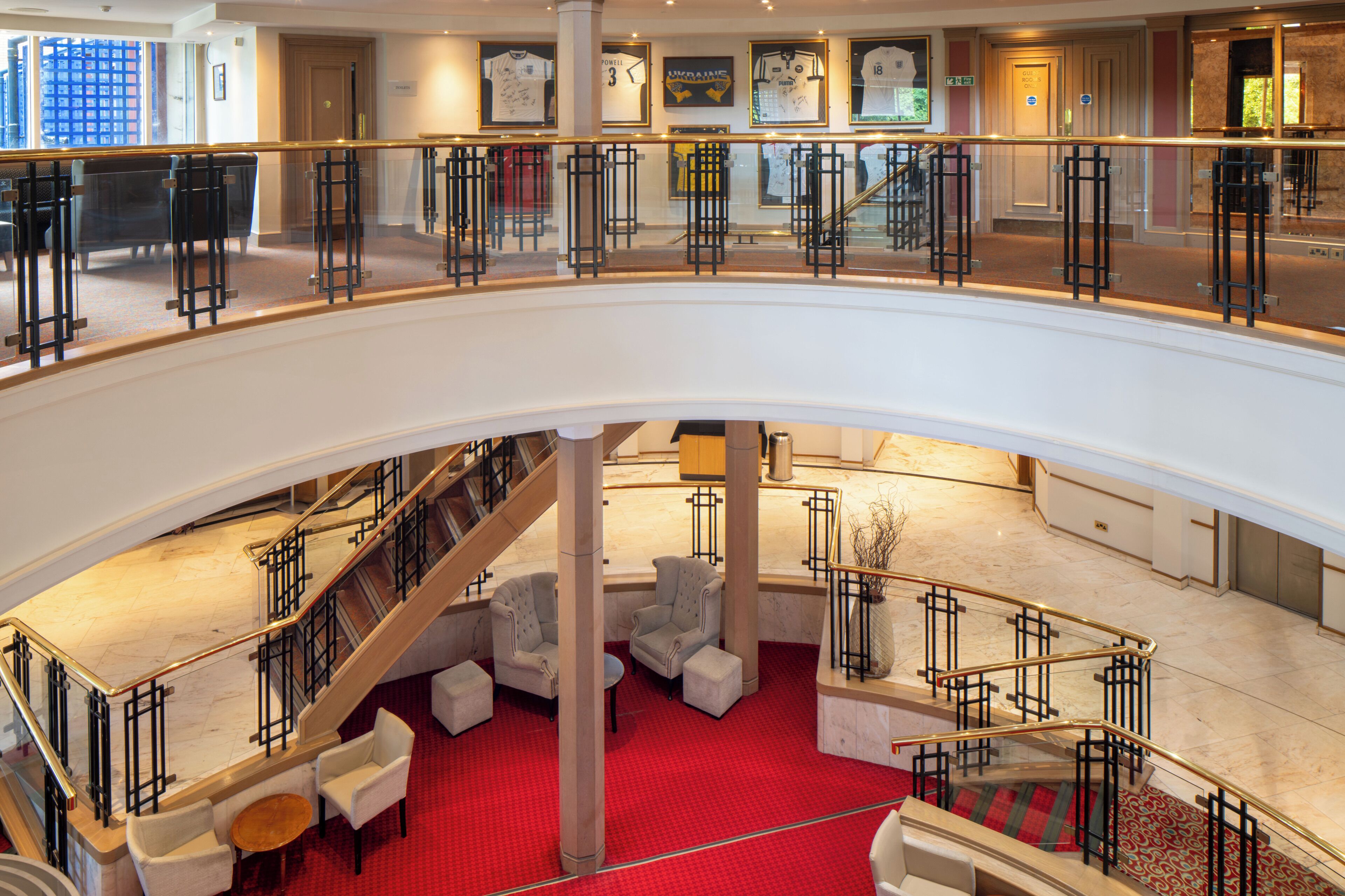 A hotel lobby with a red carpet, a staircase, and a seating area with armchairs and a coffee table.