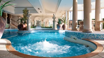 An indoor swimming pool with a hot tub, surrounded by columns and statues.