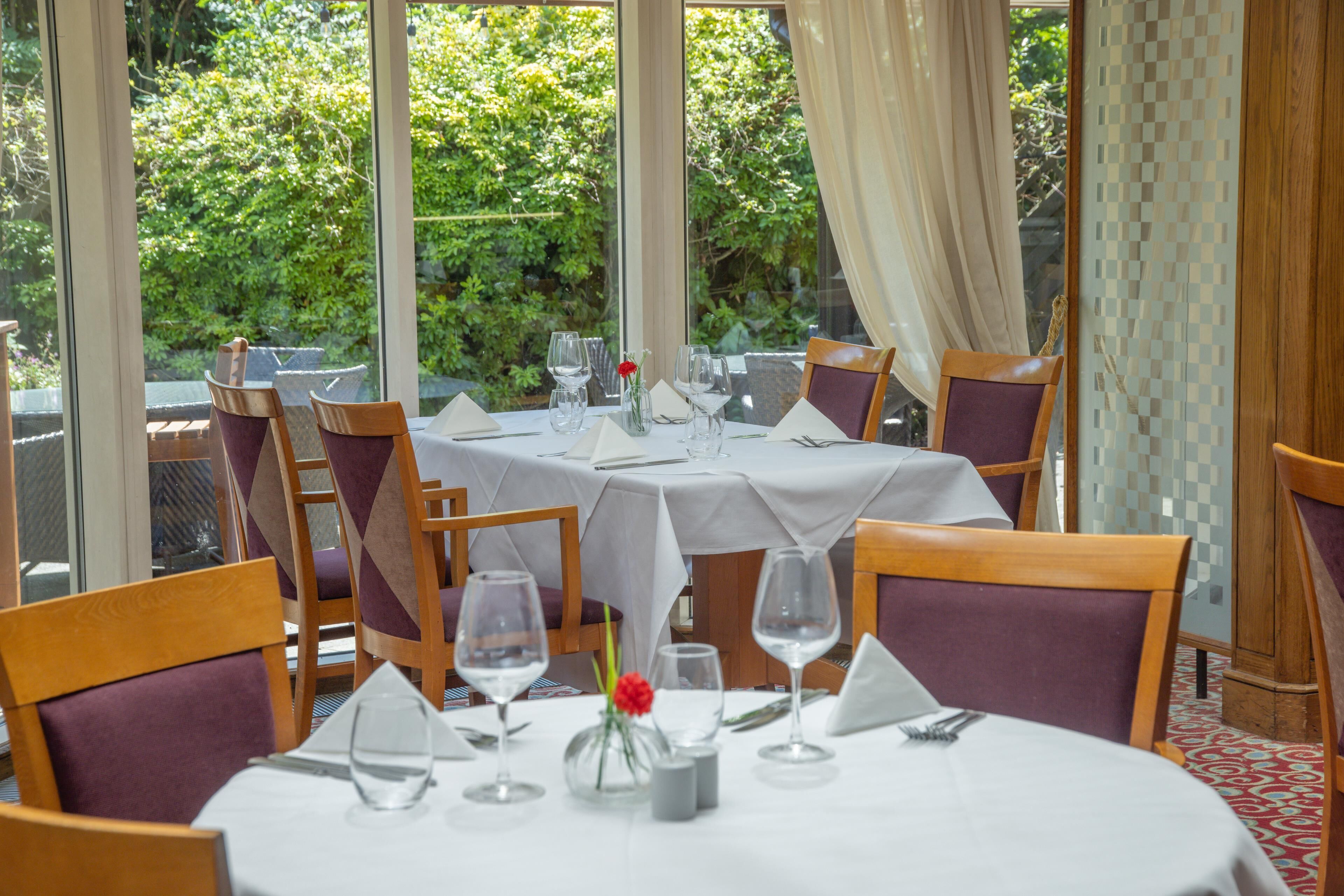A dining area with a table set for two, chairs, and a view of greenery outside.