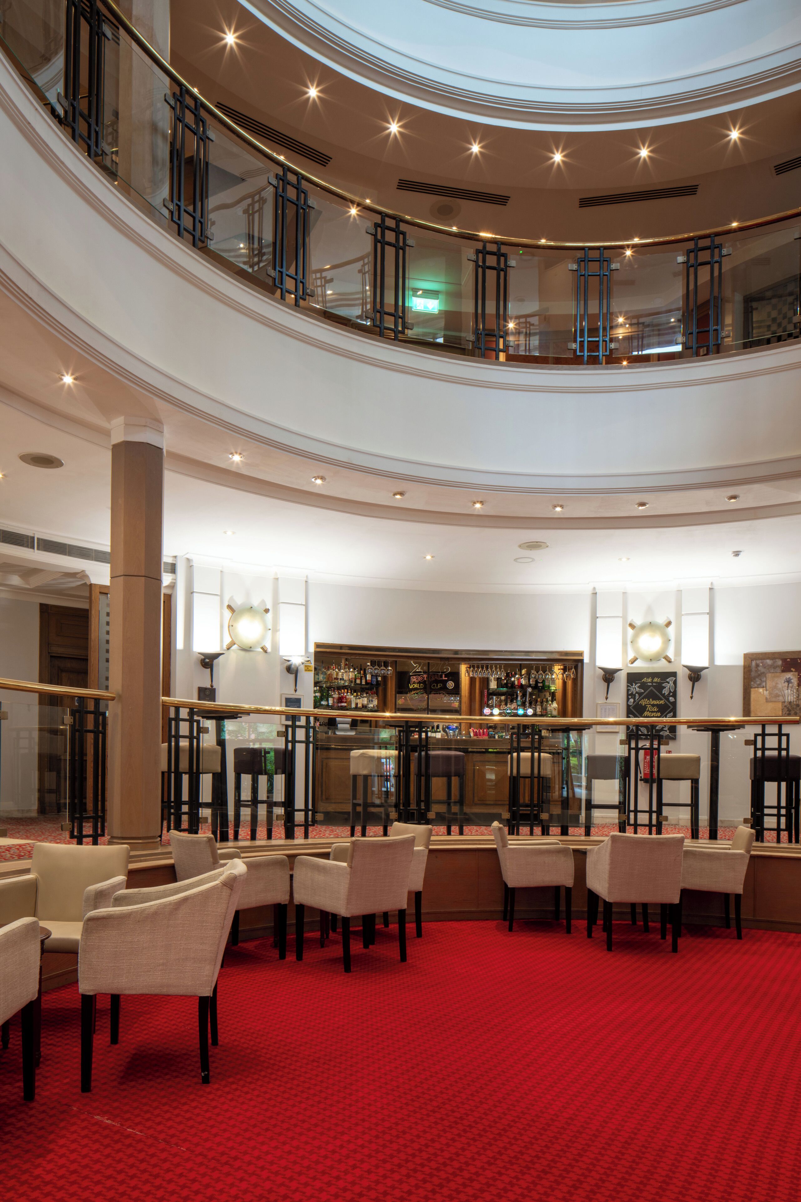 En hotellobby i flere niveauer med et rødt tæppe, siddepladser, en bar og et glasgelænder med udsigt over det nederste niveau.