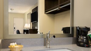 A hotel bathroom with a sink, a mirror, a coffee maker, and a basket of toiletries.