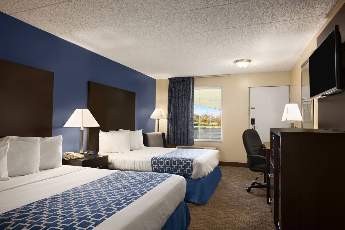 A hotel room with two beds, a desk, a chair, a TV, and a window with curtains.