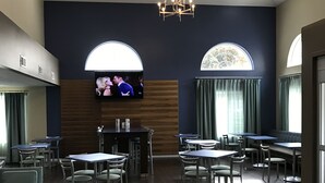 A restaurant with a modern interior, featuring a large TV screen, multiple tables and chairs, and a chandelier.