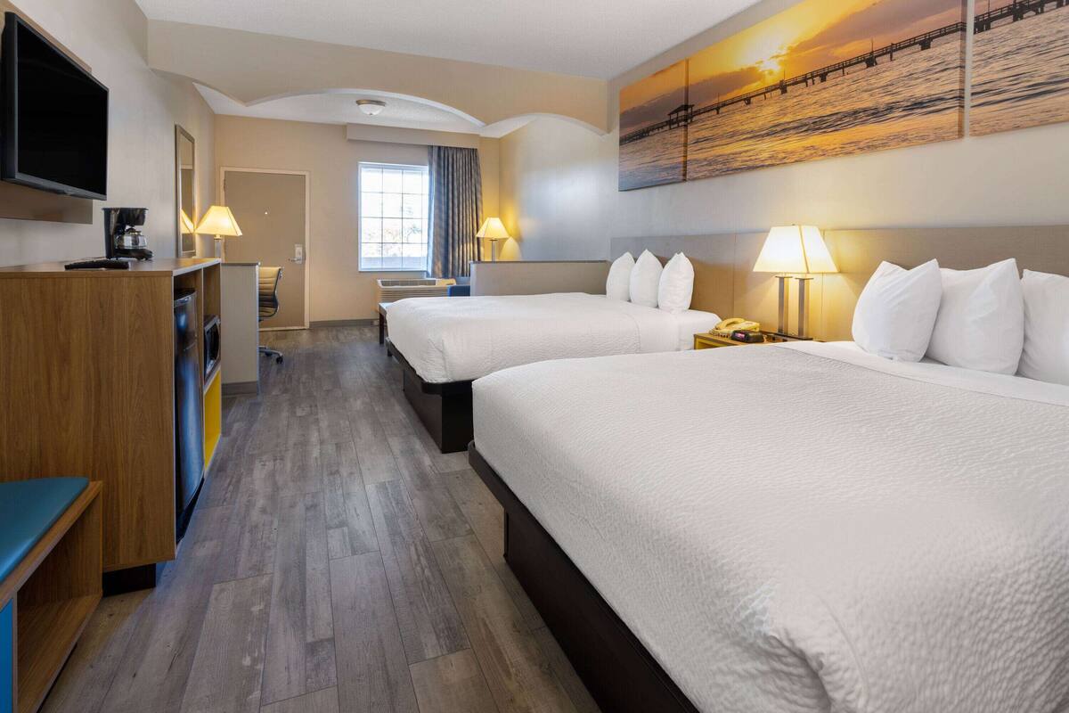 A hotel room with two beds, a TV, a desk, and a painting of a sunset over water.