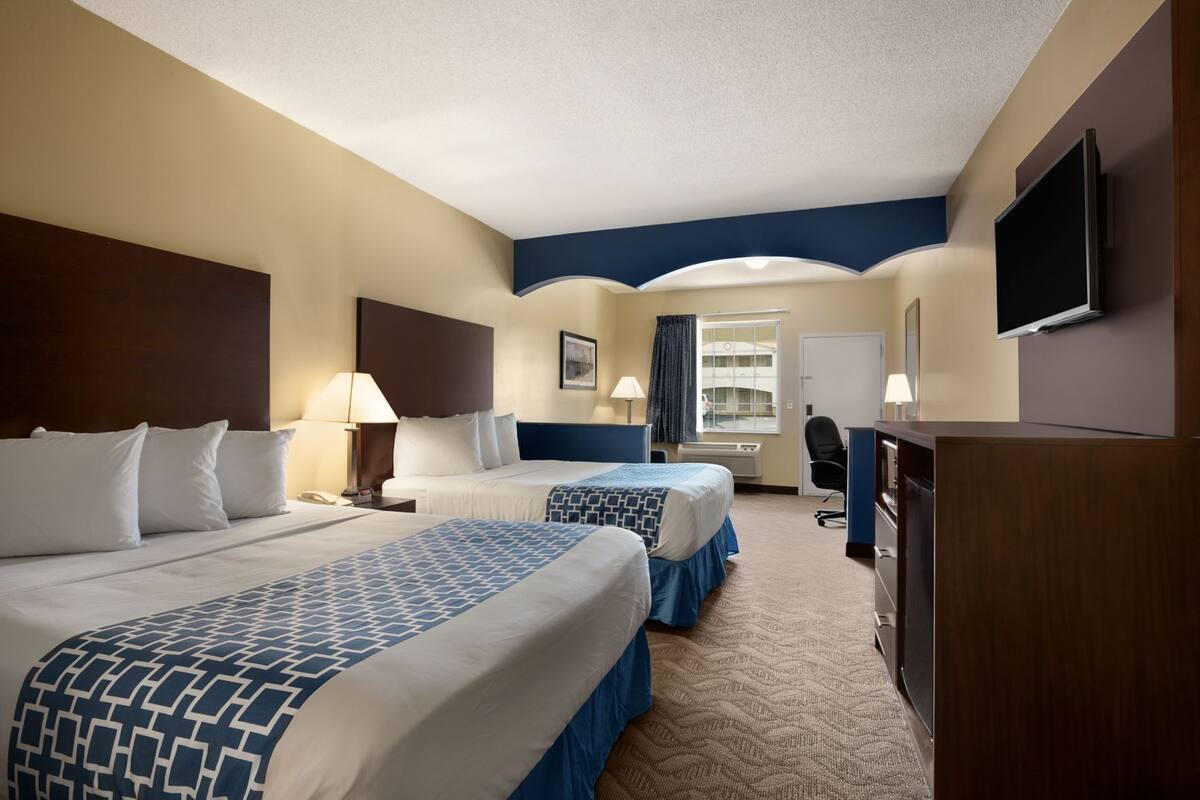 A hotel room with two beds, a desk, a chair, a television, and a window with curtains.