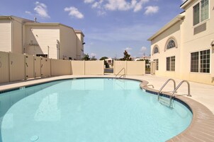 Una piscina con escalera metálica, rodeada de edificios color beige con grandes ventanales y un cielo azul despejado.