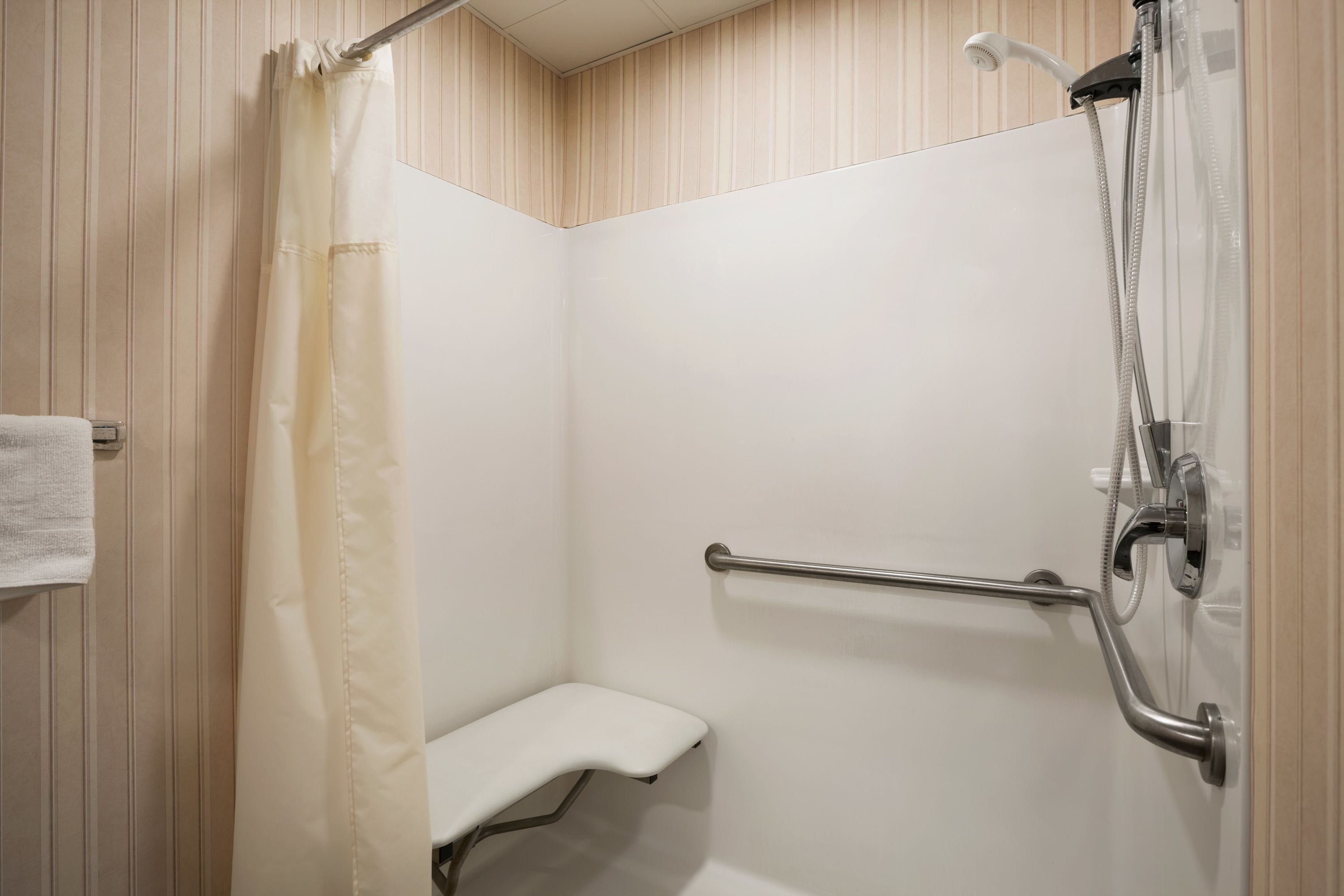Un espace douche équipé d’un banc blanc, de barres d’appui et d’un pommeau de douche.