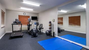 Une salle de sport équipée de matériel d’exercice, de tapis bleus et d’un grand miroir.