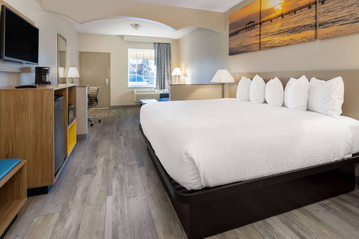 A hotel room with a large bed, a desk with a computer, a TV, and a window with curtains.