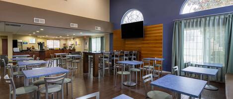 A spacious dining area with multiple tables and chairs, a counter with a cash register, and a large window with a view of trees.