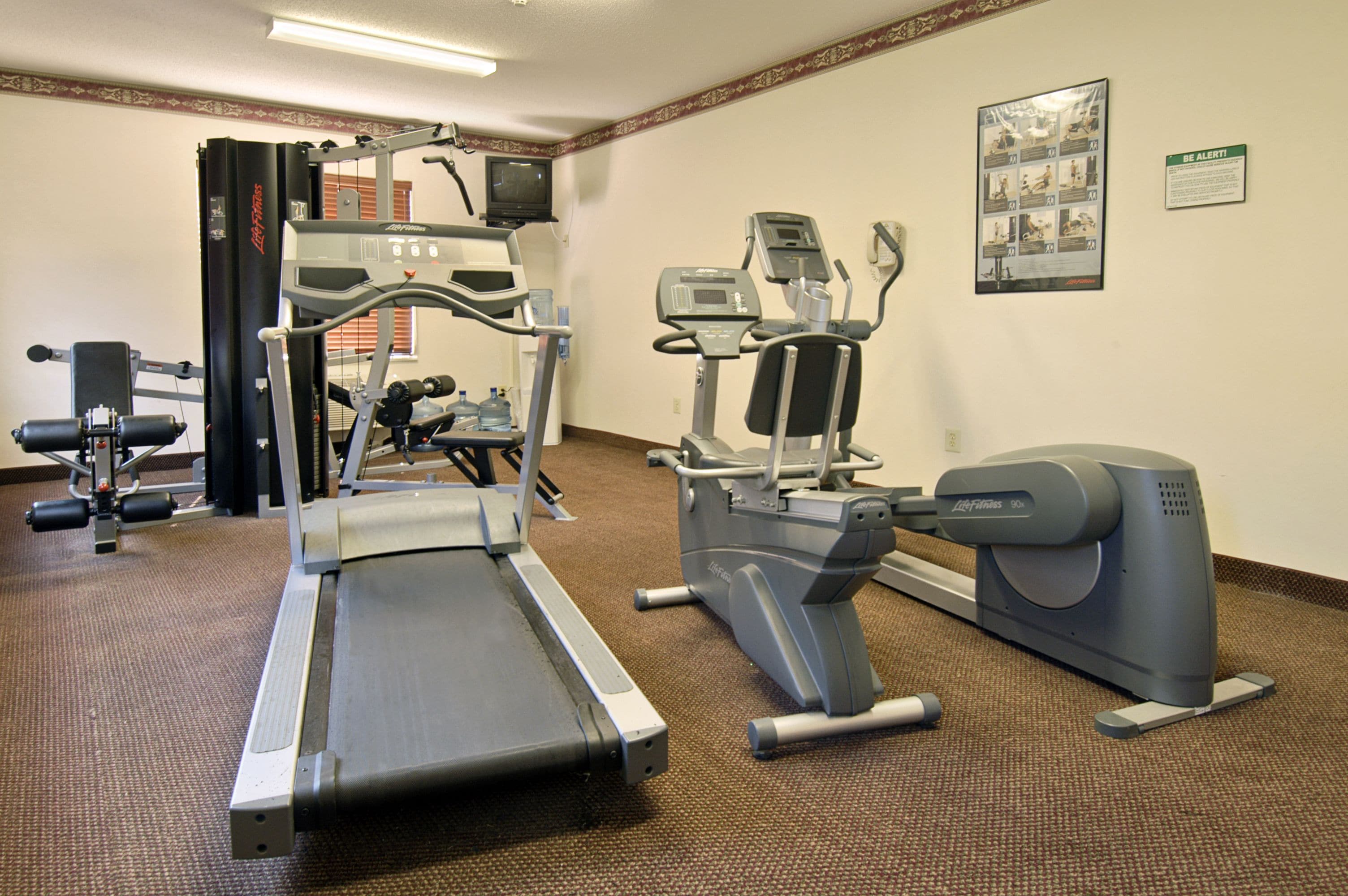 Ein Fitnessraum mit Cardiogeräten, Gewichten und einem Wasserspender.