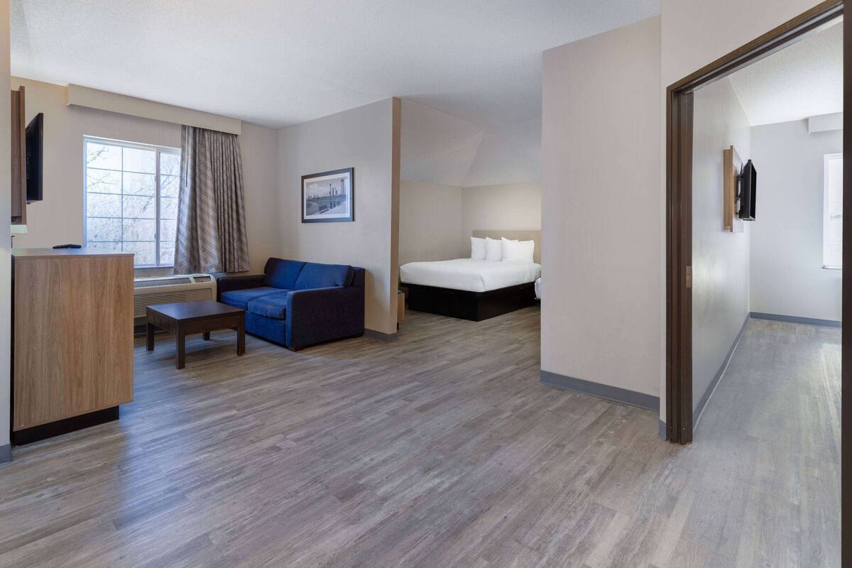 A hotel room with a wooden desk, a blue sofa, a bed with white linens, and a framed picture on the wall.
