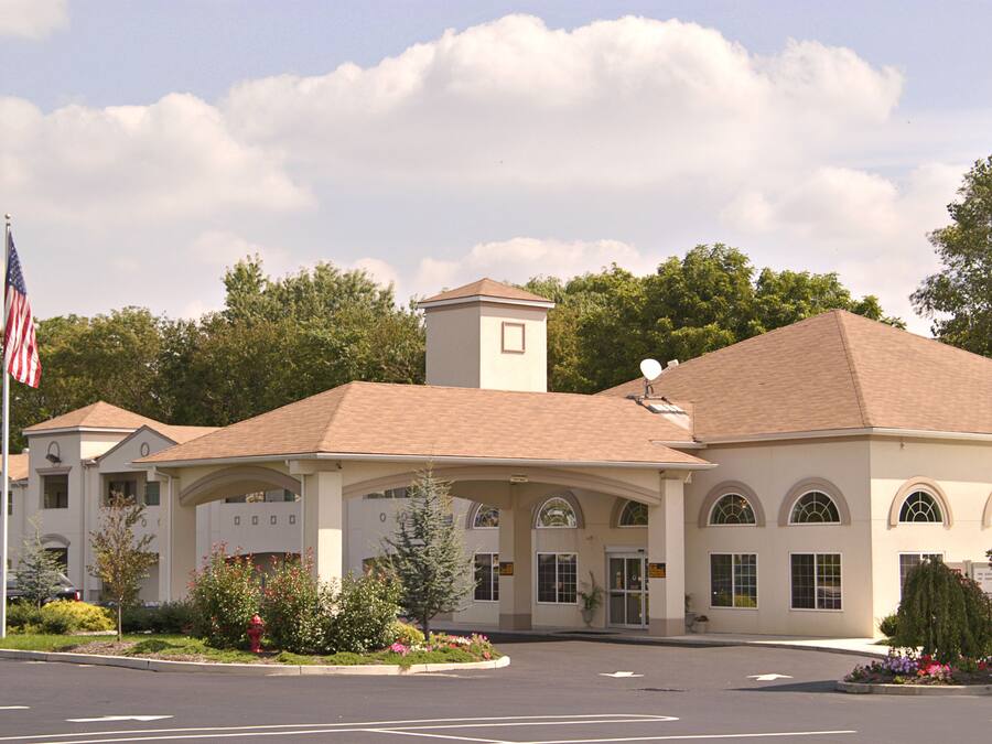A hotel with a central entrance, a flagpole with an American flag, and a parking lot.